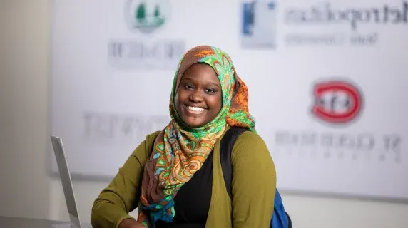 Woman smiling with university logos on the wall in the background 