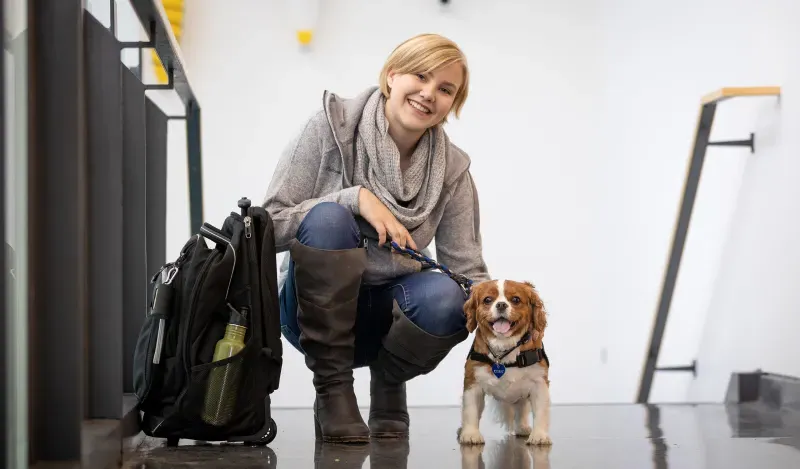 女学生微笑着蹲在一只小服务犬旁边